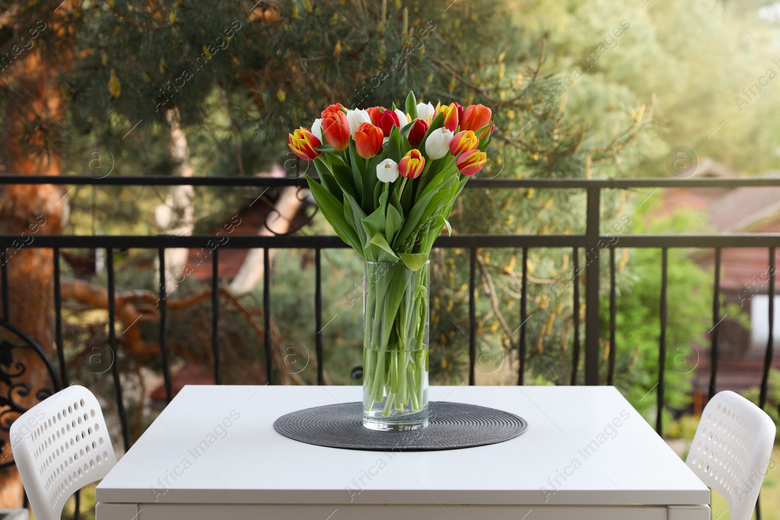 Photo of Beautiful colorful tulips in glass vase on white table at balcony