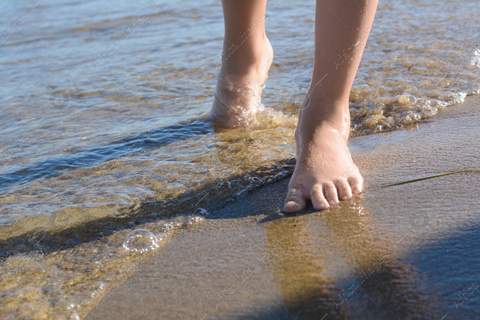 Photo of Child walking through water on seashore, closeup of legs