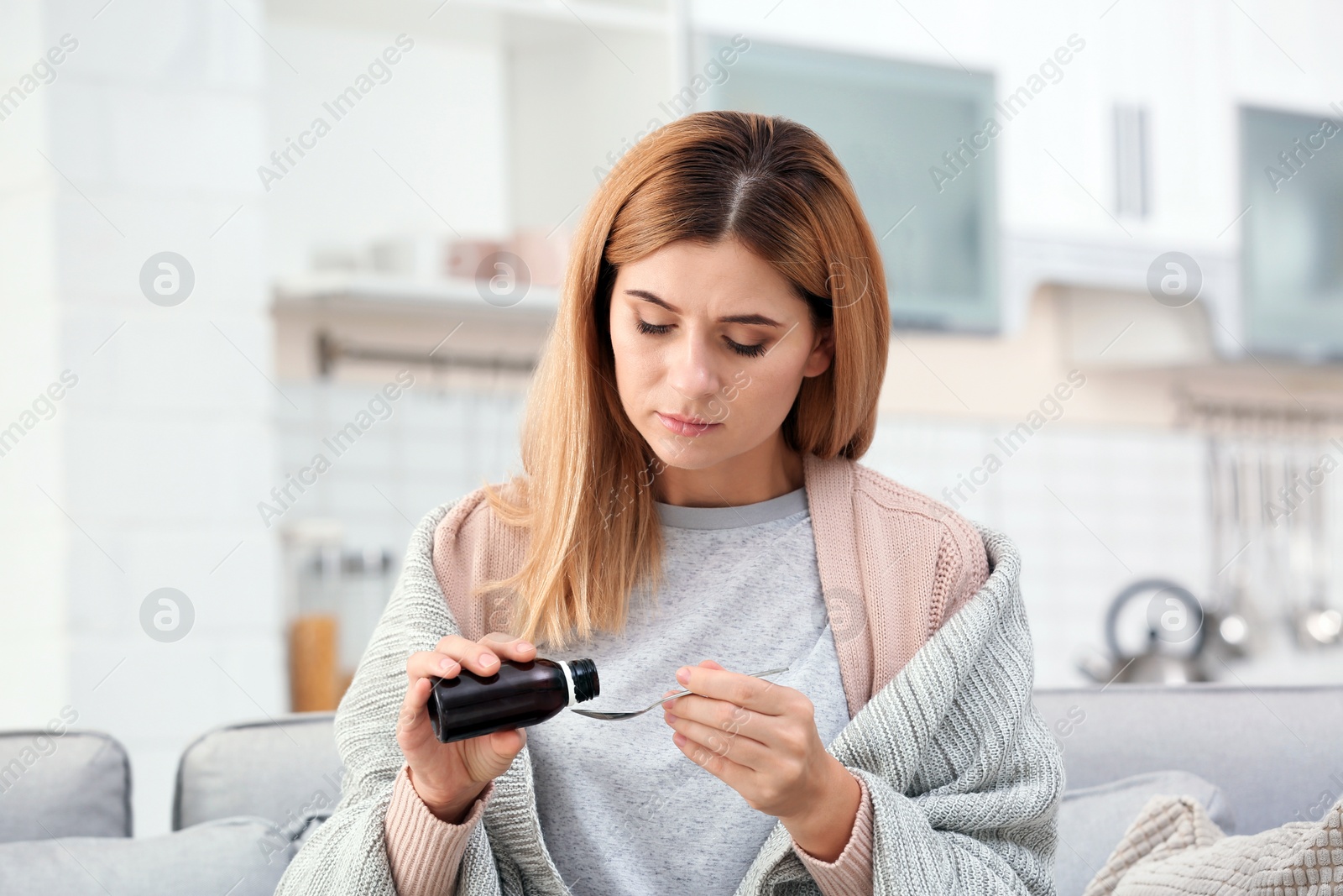 Photo of Woman taking cough syrup on sofa at home