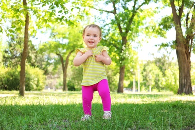 Cute baby girl learning to walk in park on sunny day