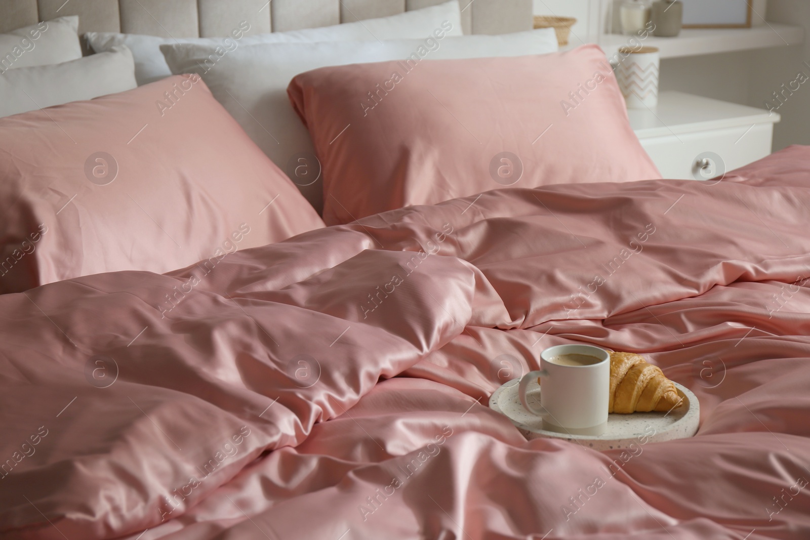 Photo of Croissant and coffee in breakfast tray on bed with beautiful pink silk linens indoors