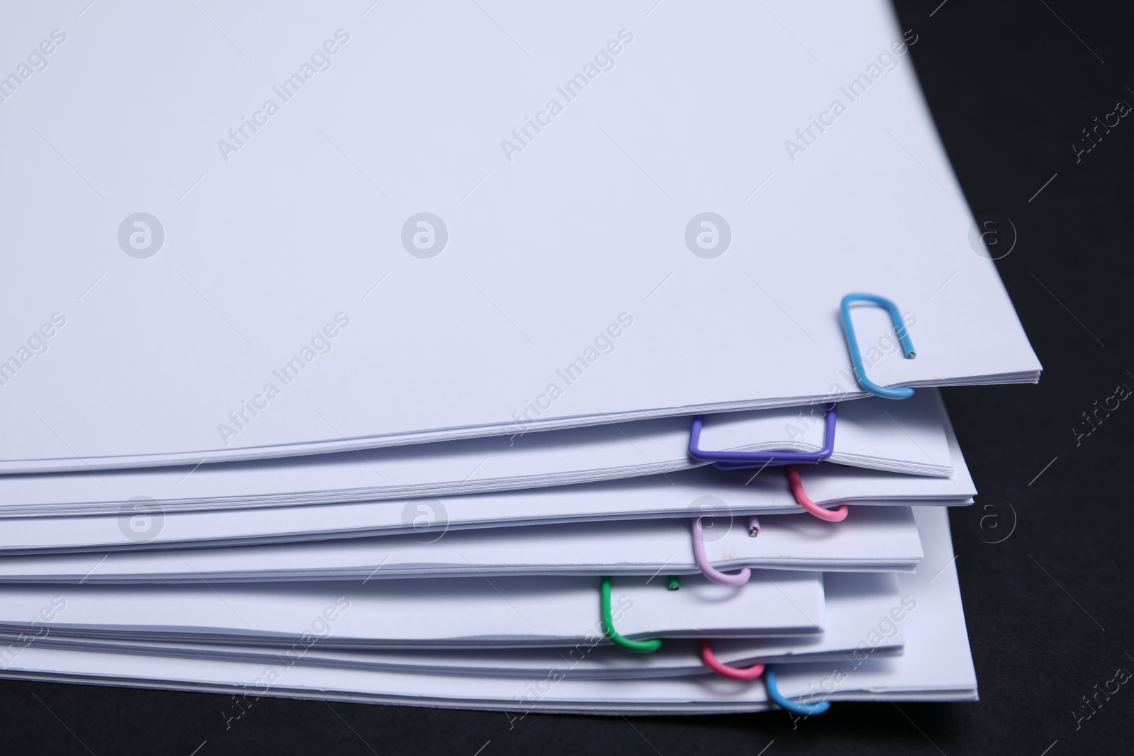 Photo of Sheets of paper with clips on black background, closeup