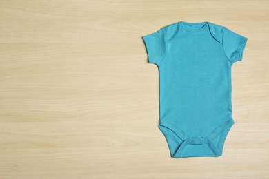 Cute baby onesie on wooden background, top view. Space for text