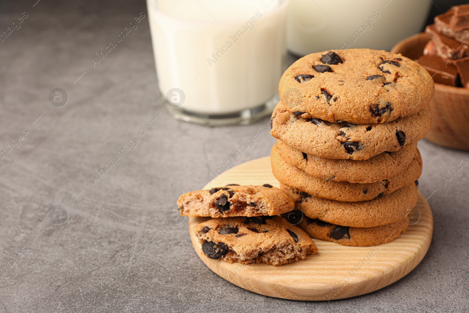 Photo of Stack of delicious chocolate chip cookies and milk on grey table. Space for text