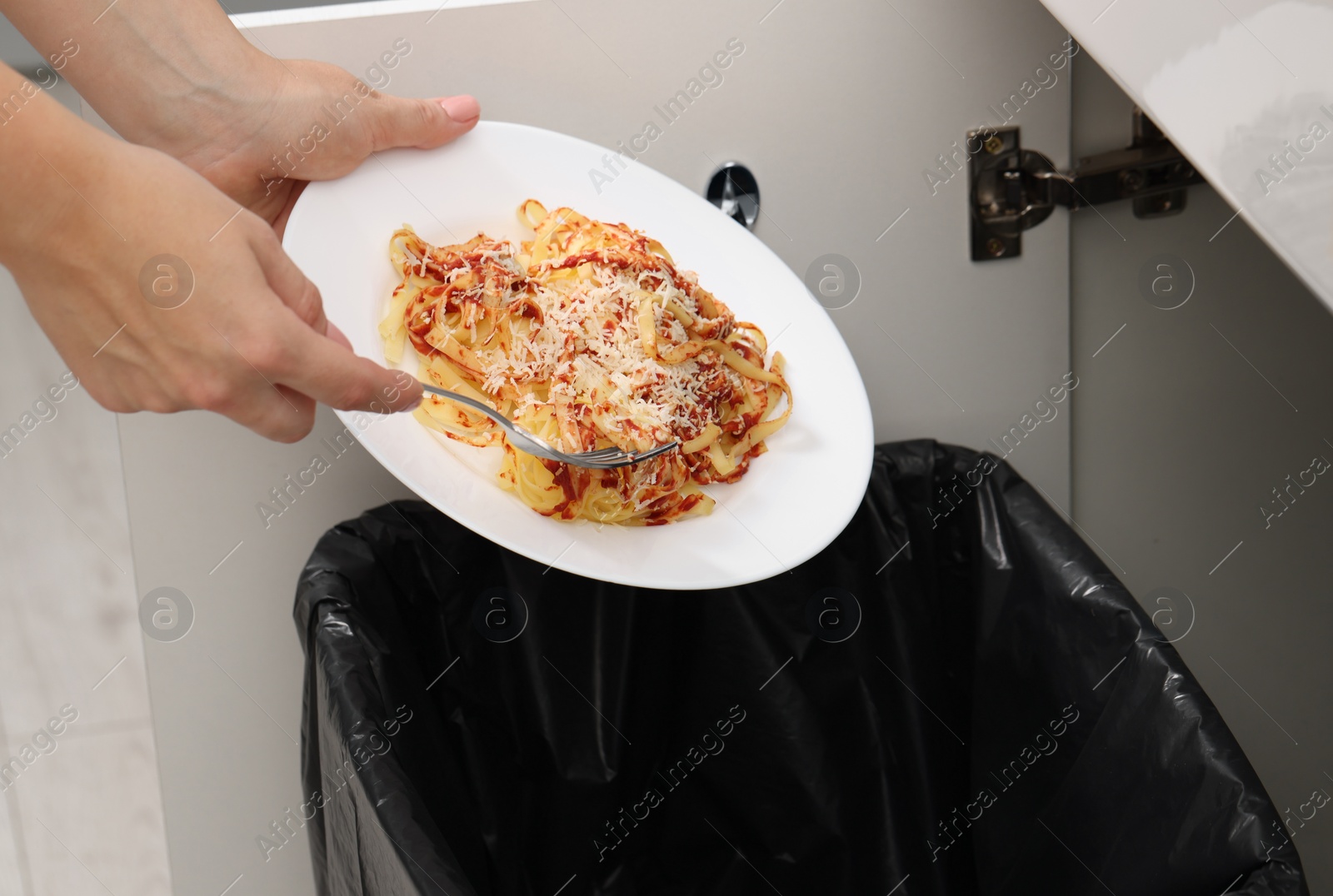 Photo of Woman throwing pasta into bin indoors, closeup