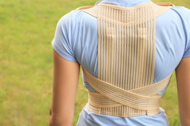 Closeup of woman with orthopedic corset on green grass outdoors, back view