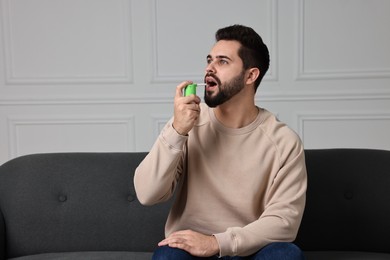 Photo of Young man using throat spray at home