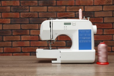 Photo of Sewing machine and spool of thread on wooden table against brick wall