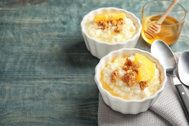 Photo of Creamy rice pudding with walnuts and orange slices in ramekins served on wooden table. Space for text