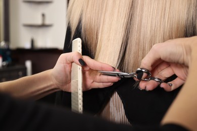 Photo of Professional hairdresser cutting woman's hair in salon, closeup