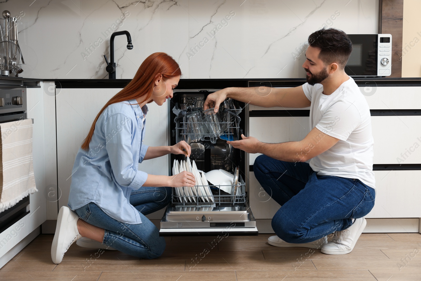 Photo of Lovely couple loading dishwasher with plates in kitchen