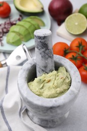 Mortar with delicious guacamole and ingredients on white table, closeup