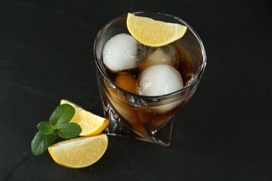 Photo of Delicious cocktail with lemon, ice balls and mint on black table