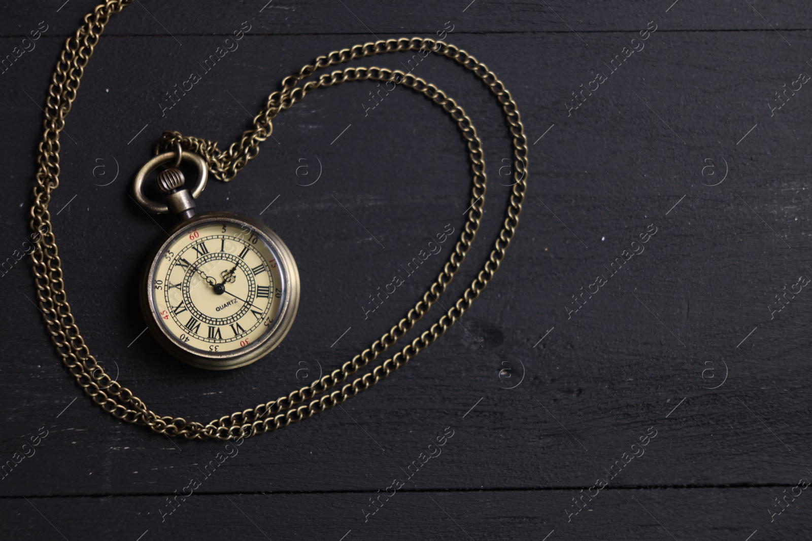 Photo of Pocket clock with chain on black wooden table, top view. Space for text