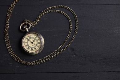 Pocket clock with chain on black wooden table, top view. Space for text