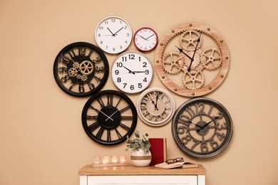 Collection of wall clocks over table with books, candles and plant indoors