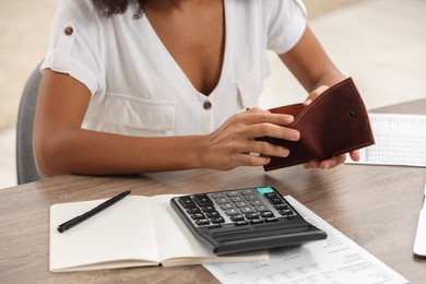 Photo of Woman with empty wallet and calculator planning budget at table indoors, closeup. Debt problem
