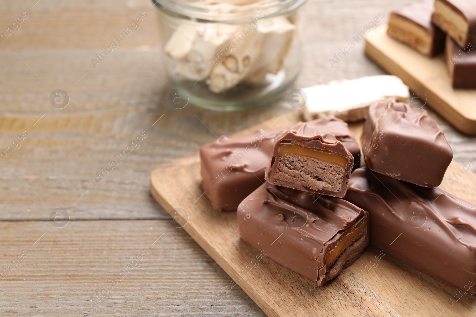 Photo of Tasty chocolate bars with nougat on wooden table, closeup. Space for text