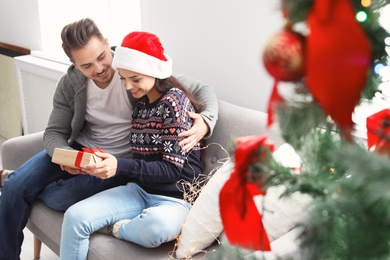 Happy young couple with Christmas gift box on sofa at home