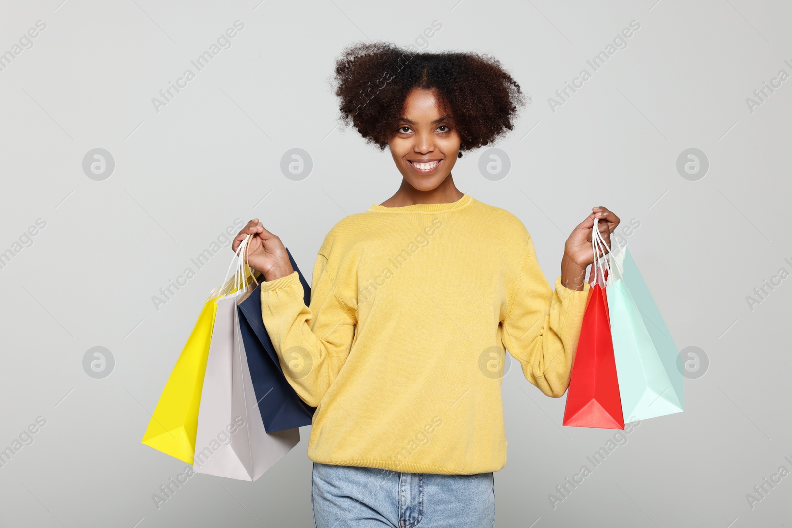 Photo of Happy African American woman with shopping bags on light grey background