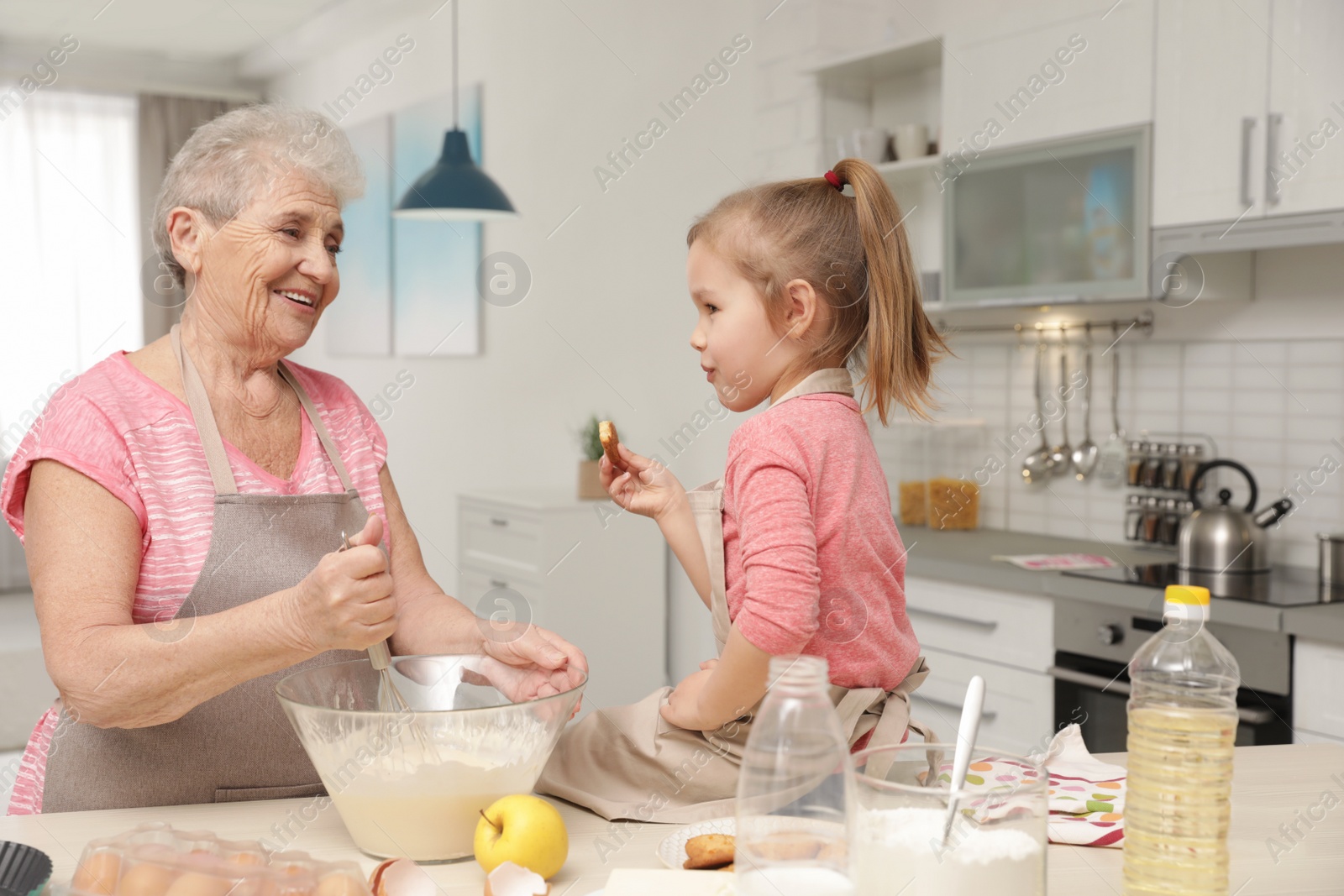 Photo of Cute girl and her grandmother cooking in kitchen