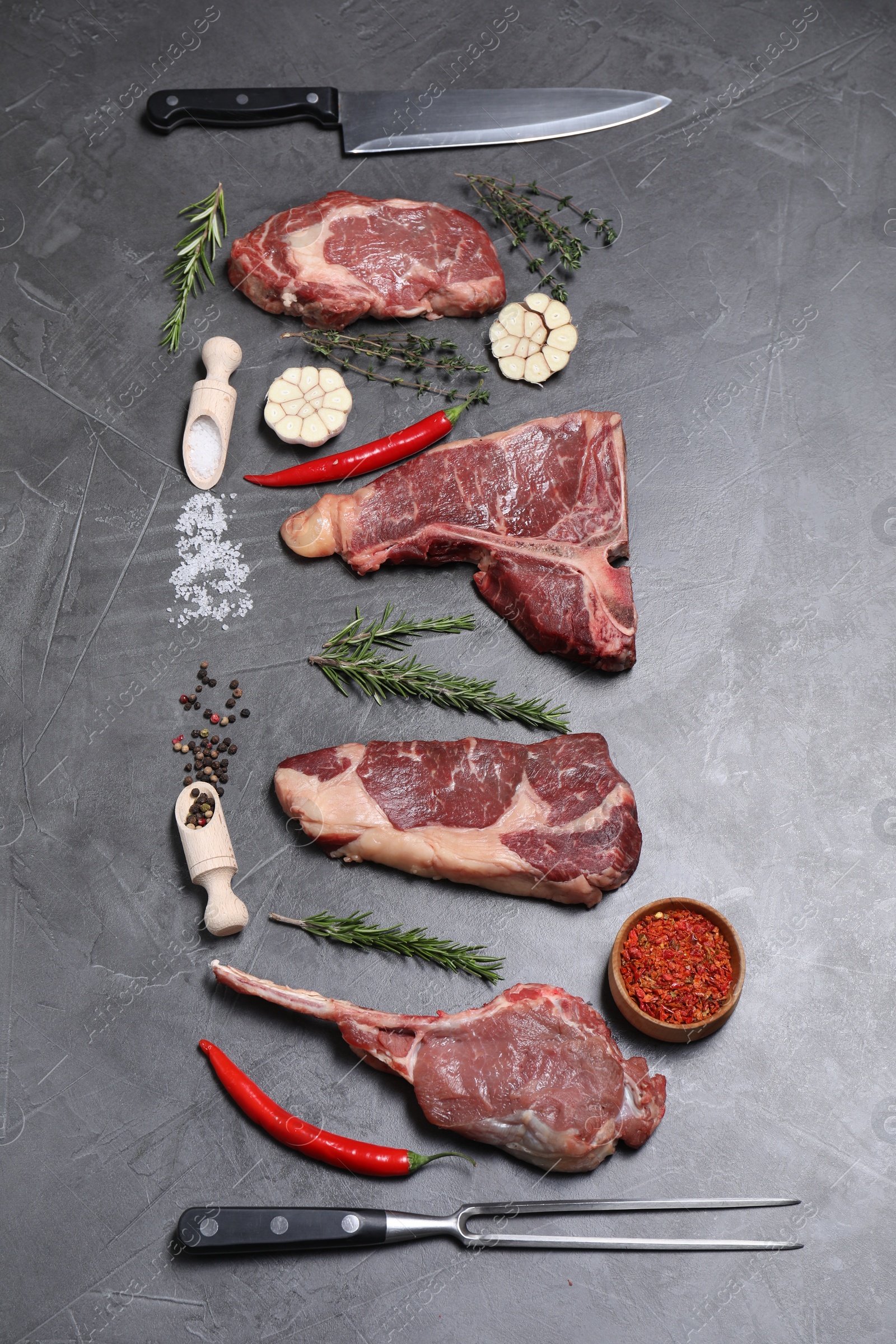 Photo of Fresh raw beef cuts, butcher tools and different spices on light grey textured table, flat lay