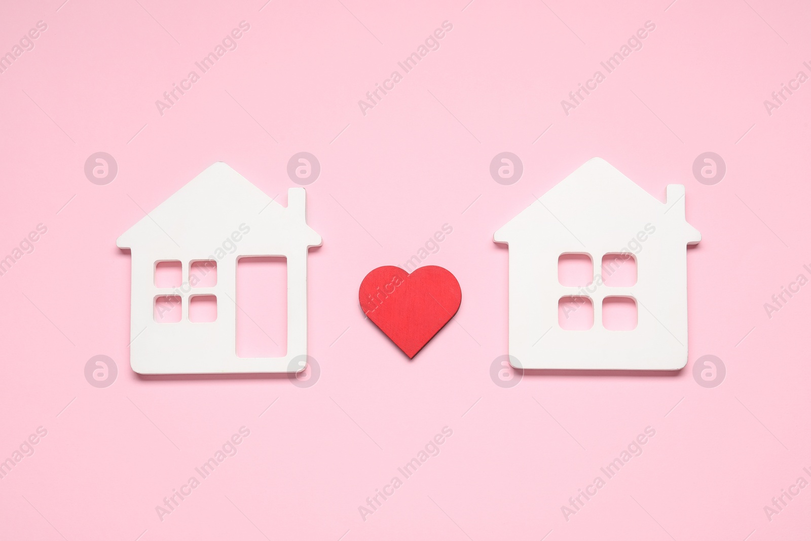 Photo of Long-distance relationship concept. Decorative heart between two white house models on pink background, flat lay