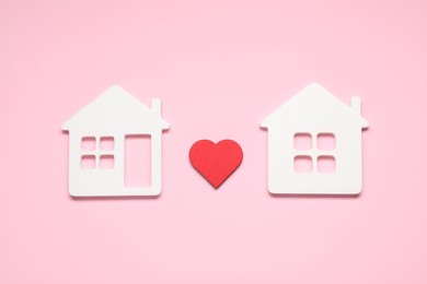 Photo of Long-distance relationship concept. Decorative heart between two white house models on pink background, flat lay