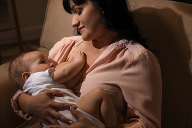 Photo of Woman breastfeeding her little baby on sofa in evening