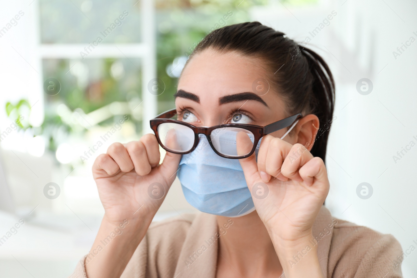 Photo of Woman wiping foggy glasses caused by wearing medical mask indoors, closeup