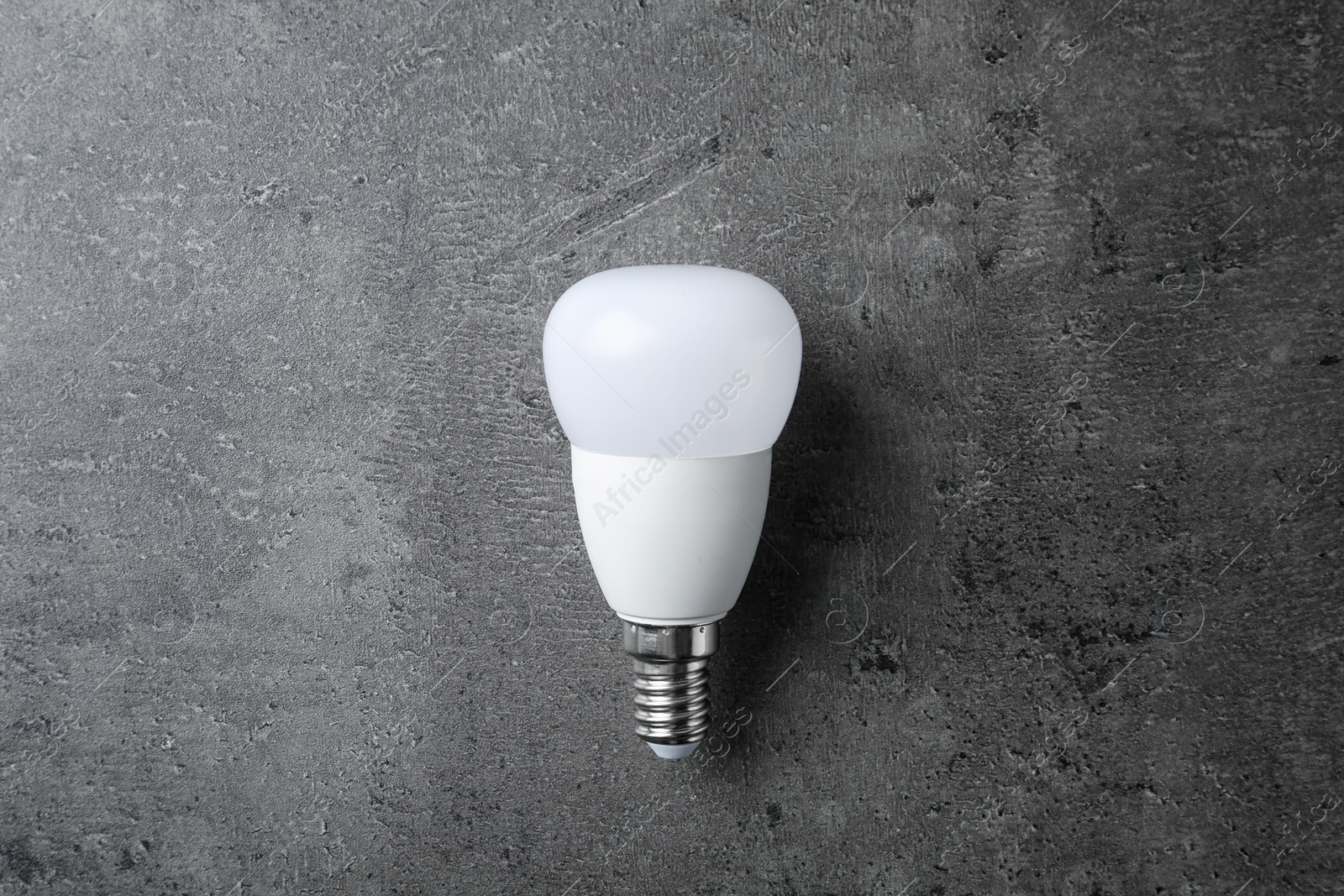 Photo of New modern lamp bulb on grey stone surface, top view