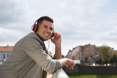 Handsome man with headphones listening to music outdoors on sunny day, space for text