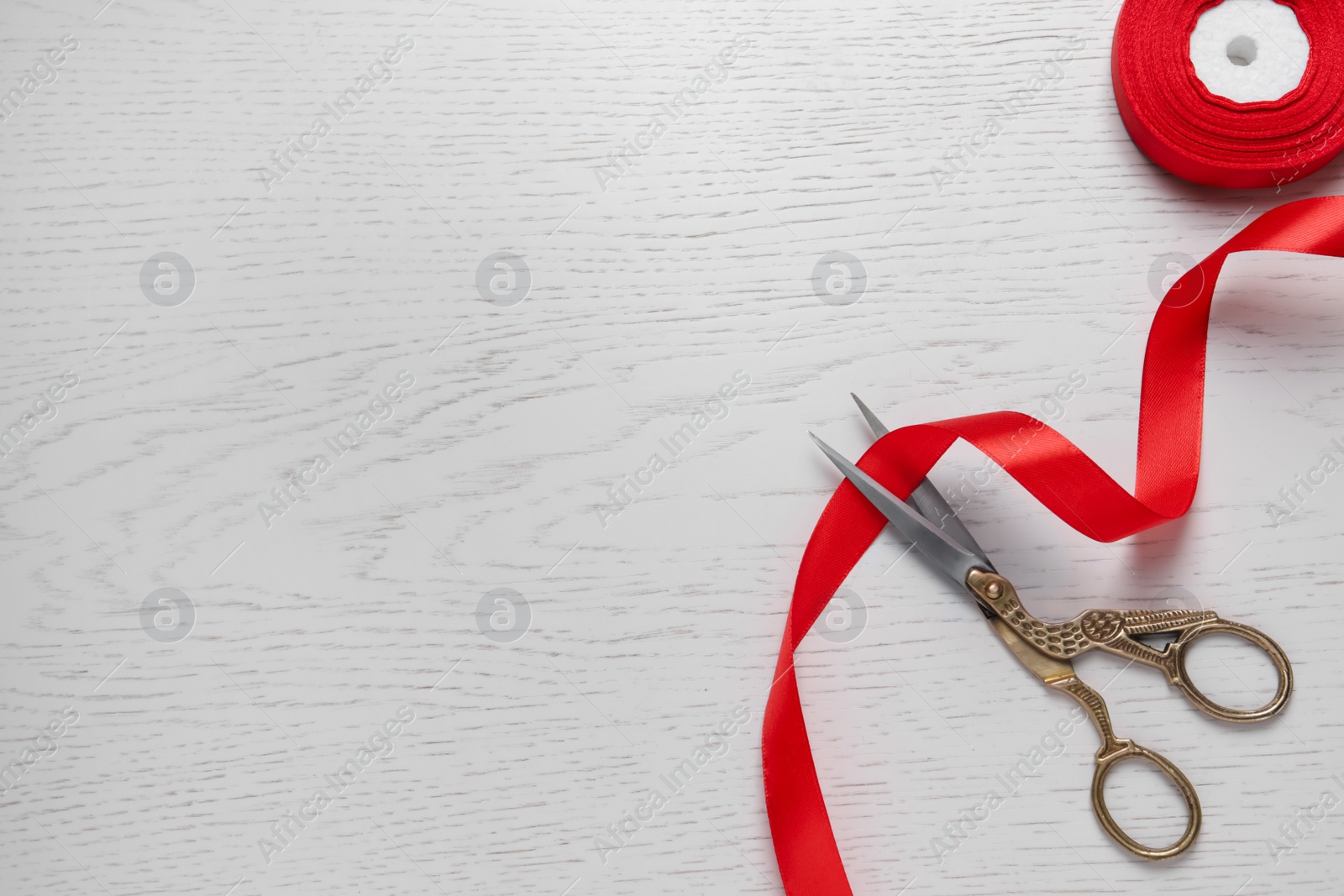 Photo of Pair of scissors with red satin ribbon on white wooden table, flat lay. Space for text