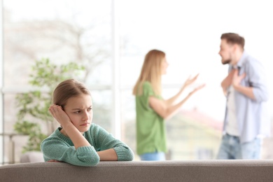 Little unhappy girl sitting on sofa while parents arguing at home