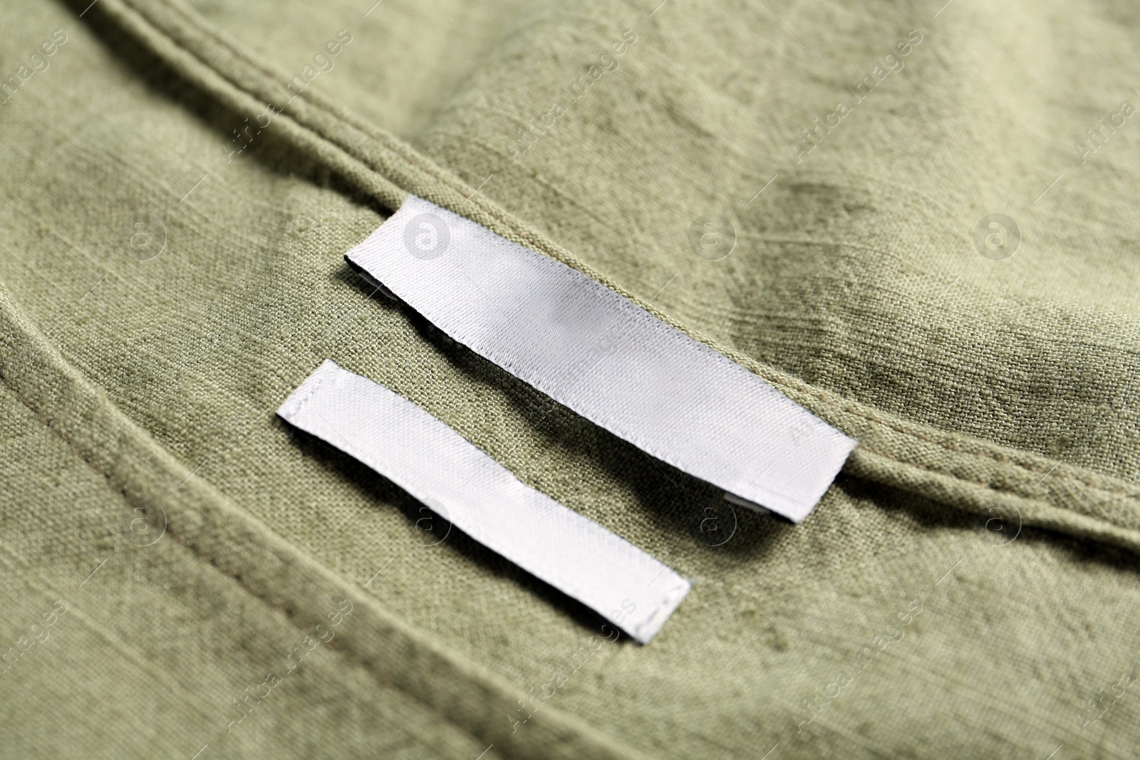 Photo of Blank clothing label on green apparel, closeup