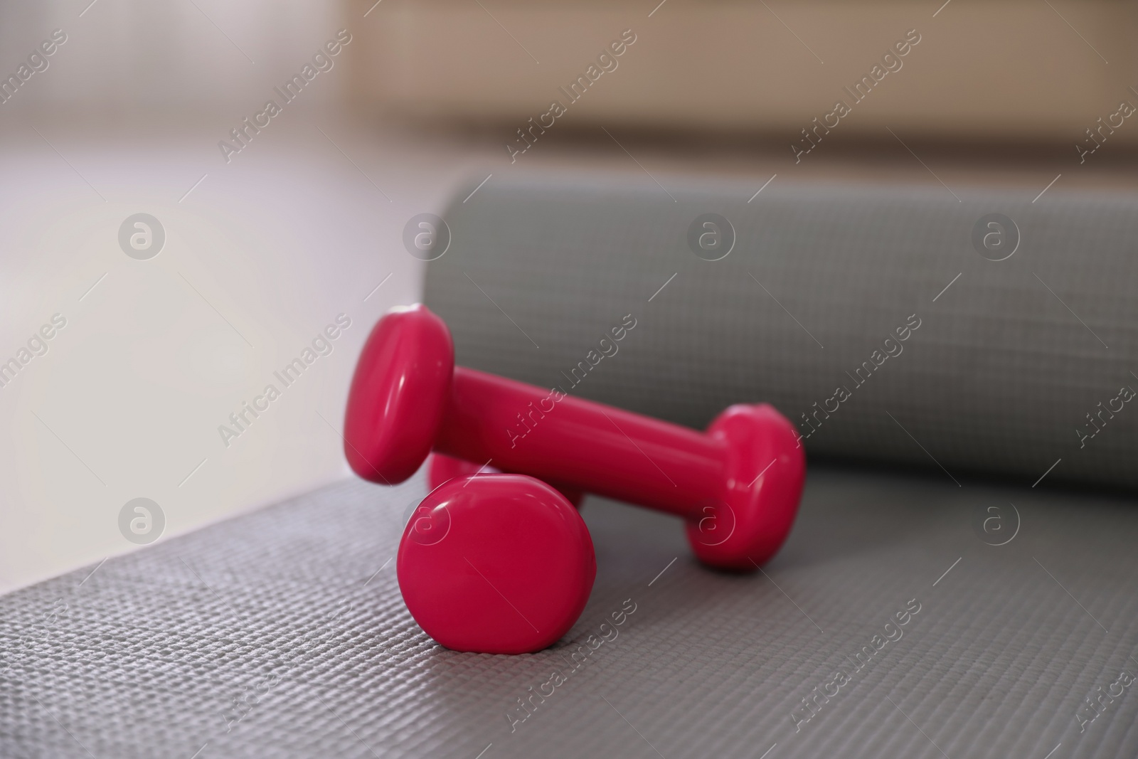 Photo of Pink dumbbells with grey yoga mat on floor in room. Home fitness