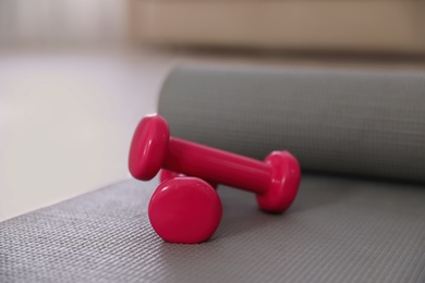 Photo of Pink dumbbells with grey yoga mat on floor in room. Home fitness