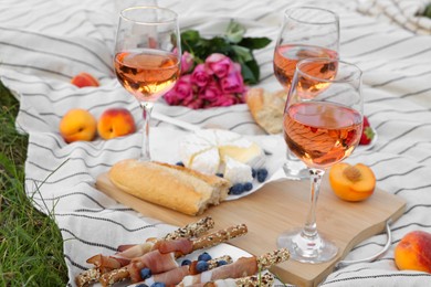 Glasses of delicious rose wine, flowers and food on picnic blanket outdoors