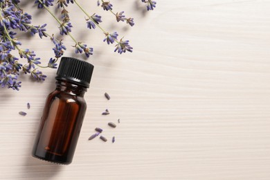 Bottle of essential oil and lavender flowers on white wooden table, flat lay. Space for text