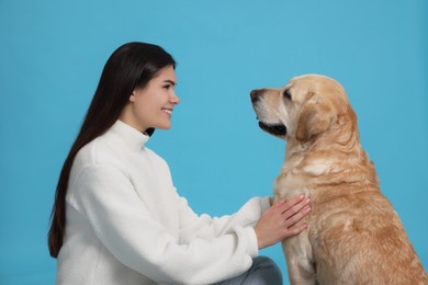 Photo of Happy woman with cute Labrador Retriever on light blue background
