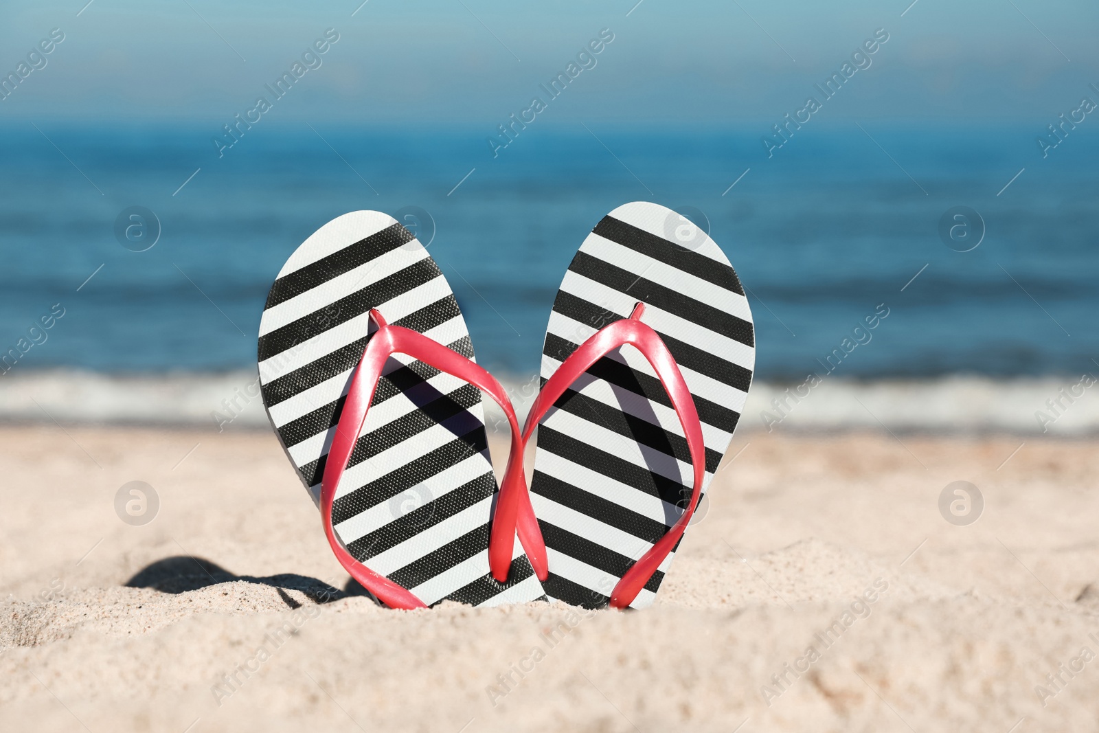 Photo of Striped flip flops in sand on beach near sea