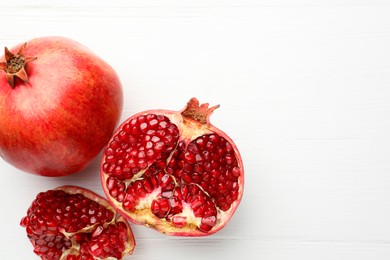 Fresh pomegranates on white wooden table, top view. Space for text