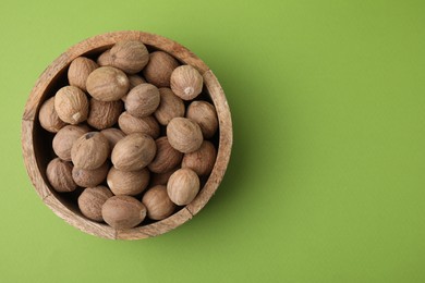 Photo of Whole nutmegs in bowl on light green background, top view. Space for text