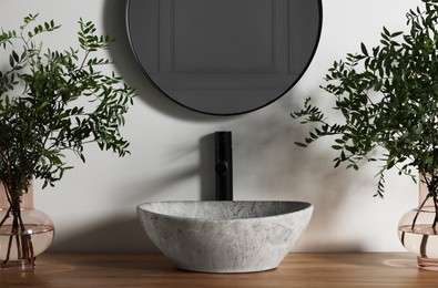 Photo of Eucalyptus branches near vessel sink on bathroom vanity. Interior design