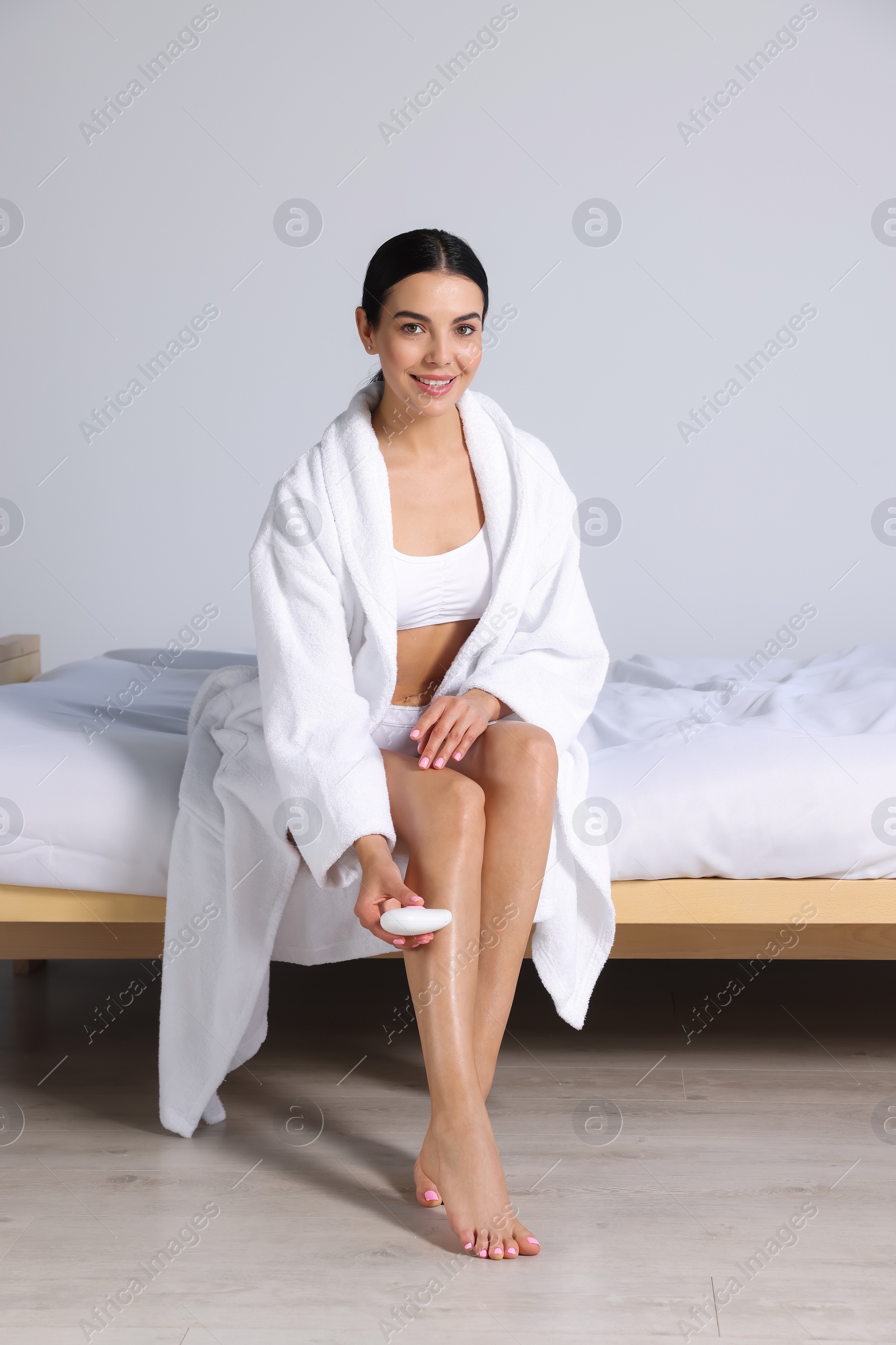 Photo of Young woman epilating her legs in bedroom