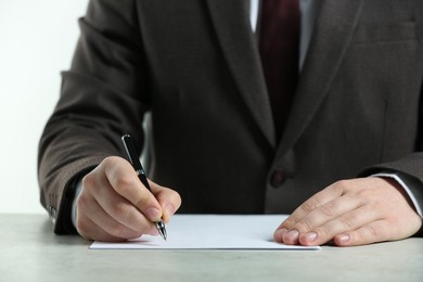 Photo of Man writing on sheet of paper with pen at white table, closeup