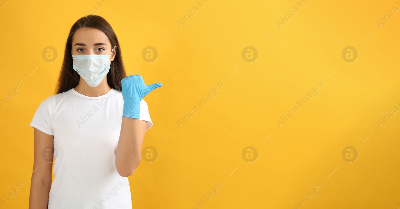 Photo of Woman in protective face mask and medical gloves pointing at something on yellow background. Space for text