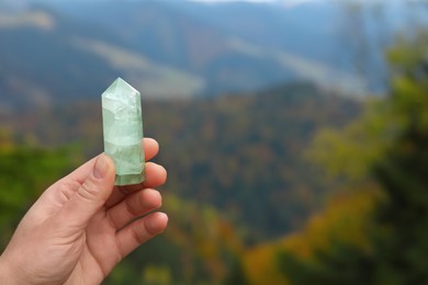 Photo of Woman holding crystal in mountains, closeup. Space for text