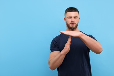 Photo of Man showing time out gesture on light blue background, space for text