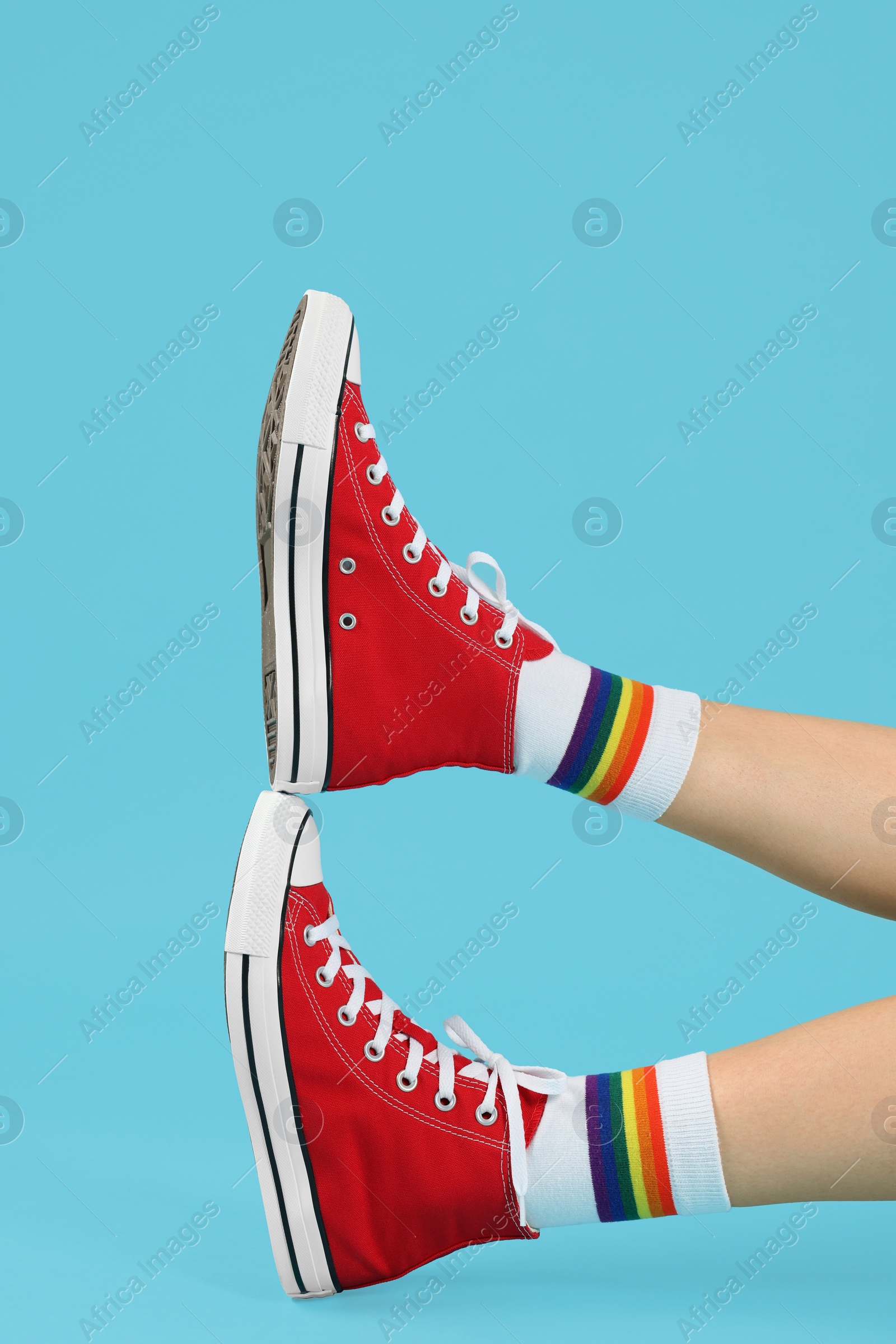 Photo of Woman in stylish gumshoes on light blue background, closeup